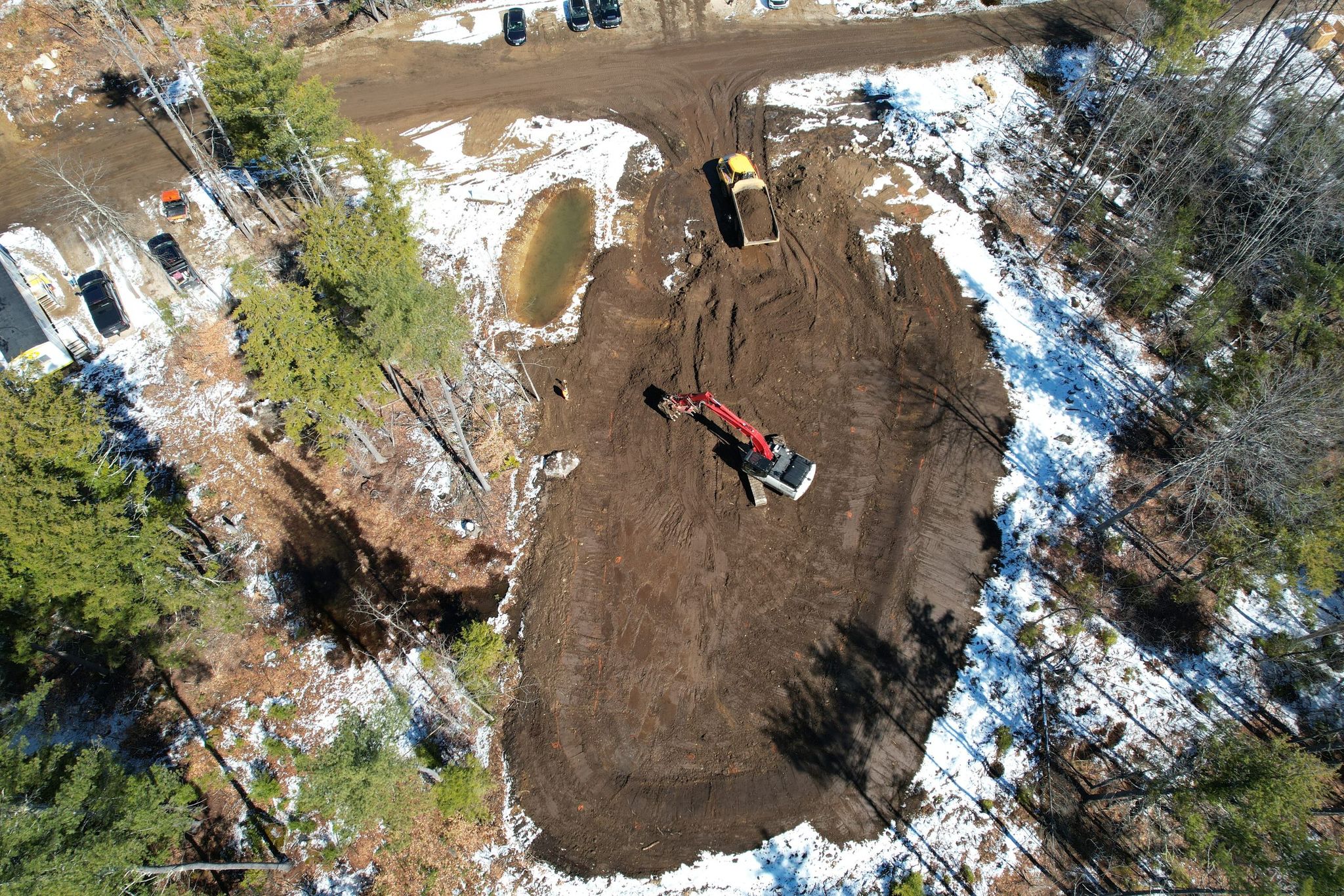 Aerial view looking down into a deep excavation, with an excavator and haul truck working in the cut.