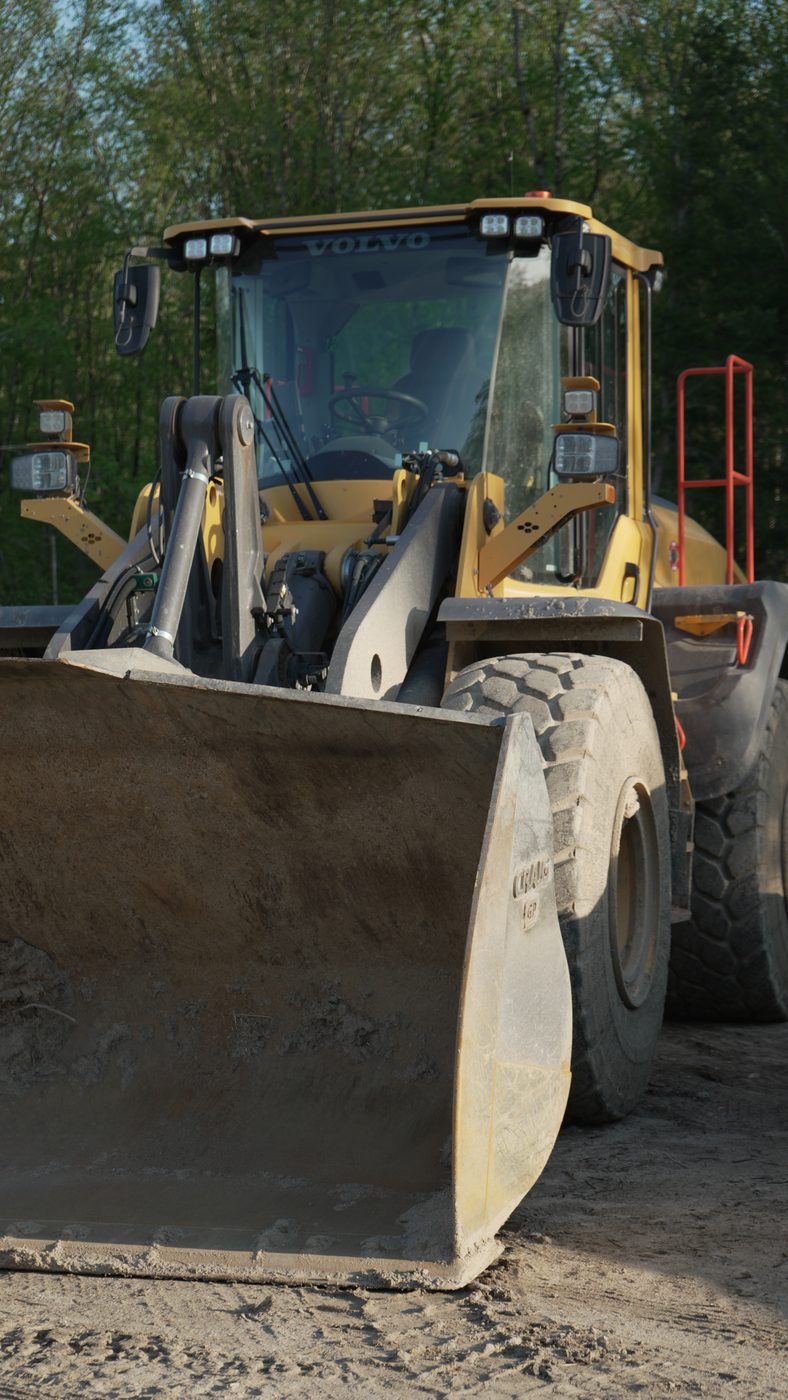 A wheel loader at close range, bucket edge and lift arms in the foreground.